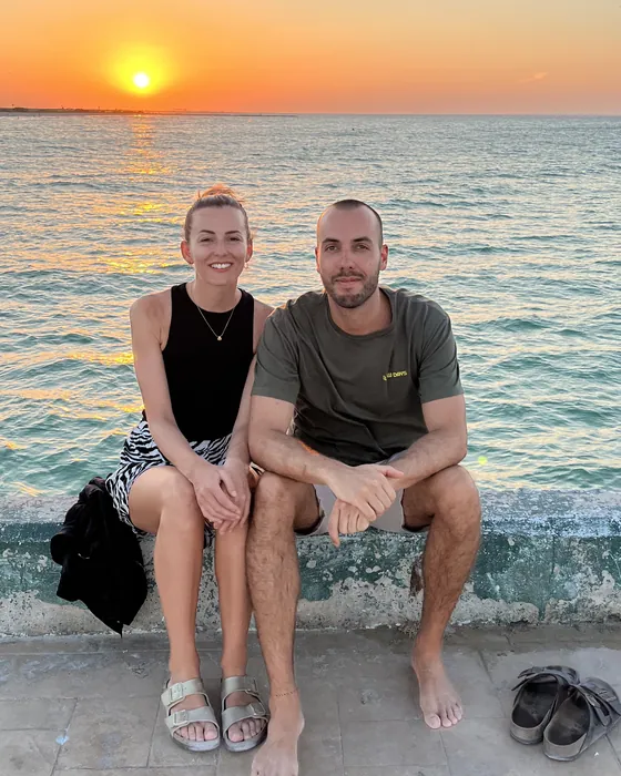 Bianca und Alex auf der Hafenmauer einer Local Island, dahinter das Meer im Abendlicht
